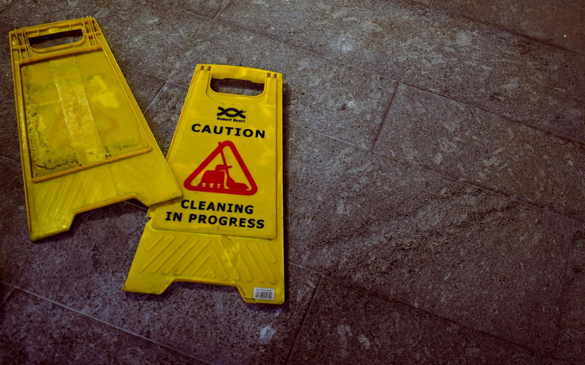 Yellow folding sign on a tiled floor reading CAUTION — CLEANING IN PROGRESS.