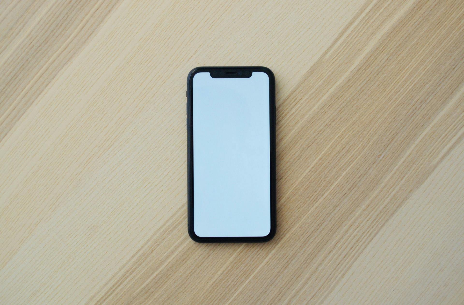 Smartphone with a blank illuminated screen lying on a wooden surface.