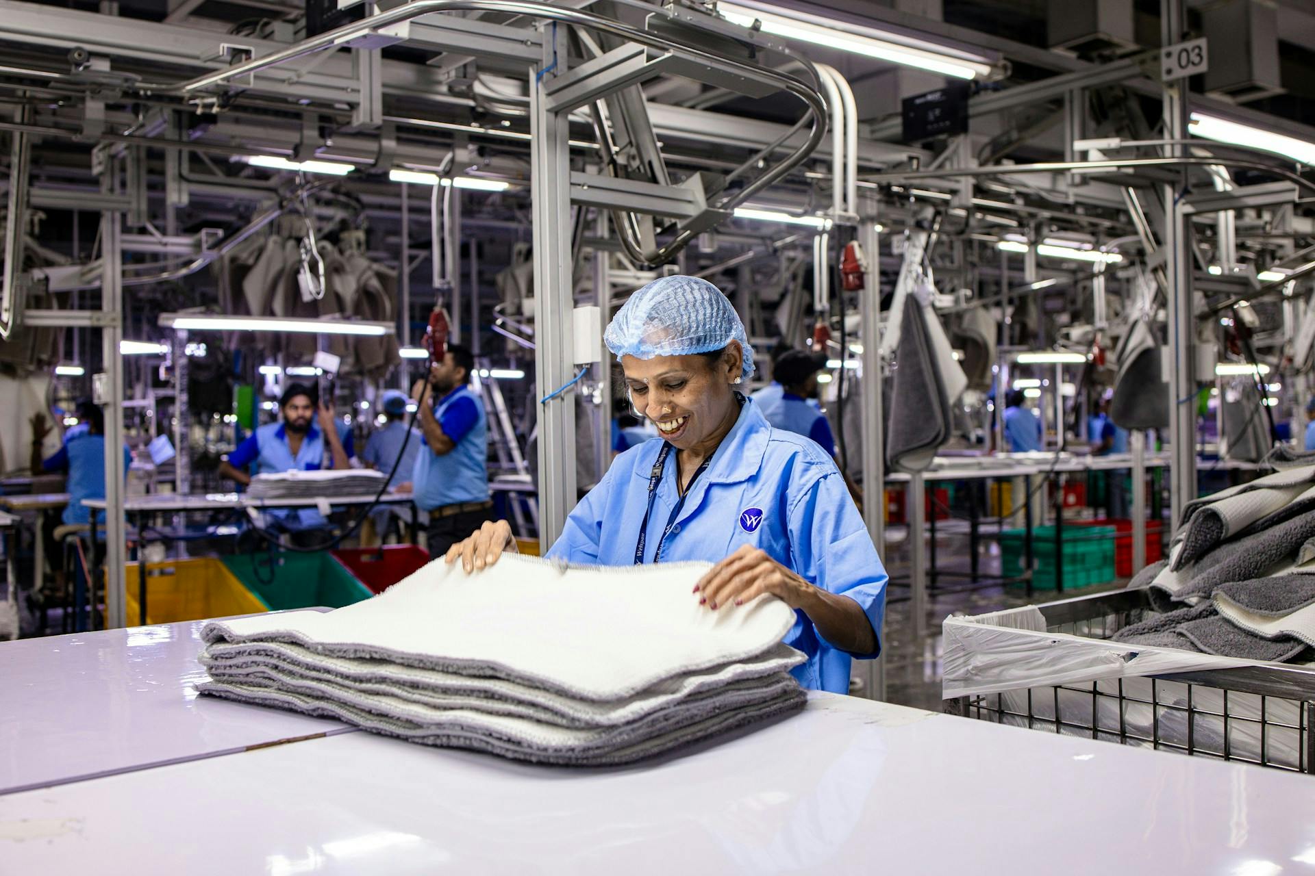Smiling factory worker in a blue uniform and hairnet stacking layered material on a worktable.