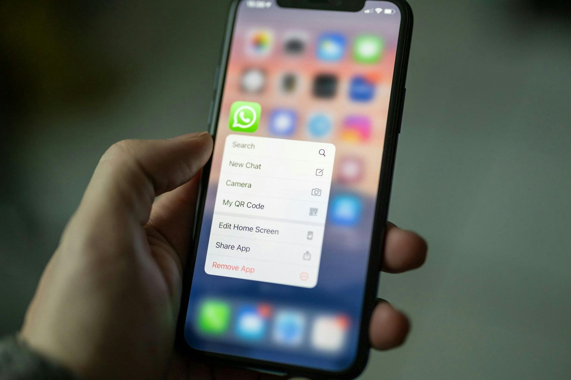 Hand holding a smartphone with the WhatsApp shortcut menu open.