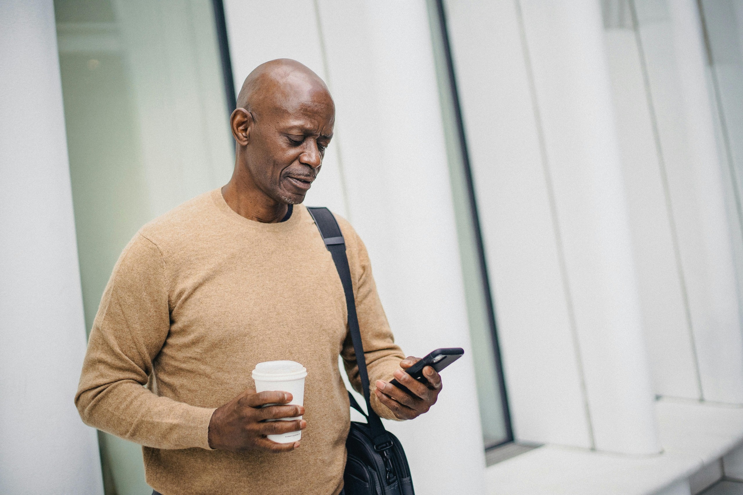 Man looking at a smartphone while holding a takeaway coffee cup.