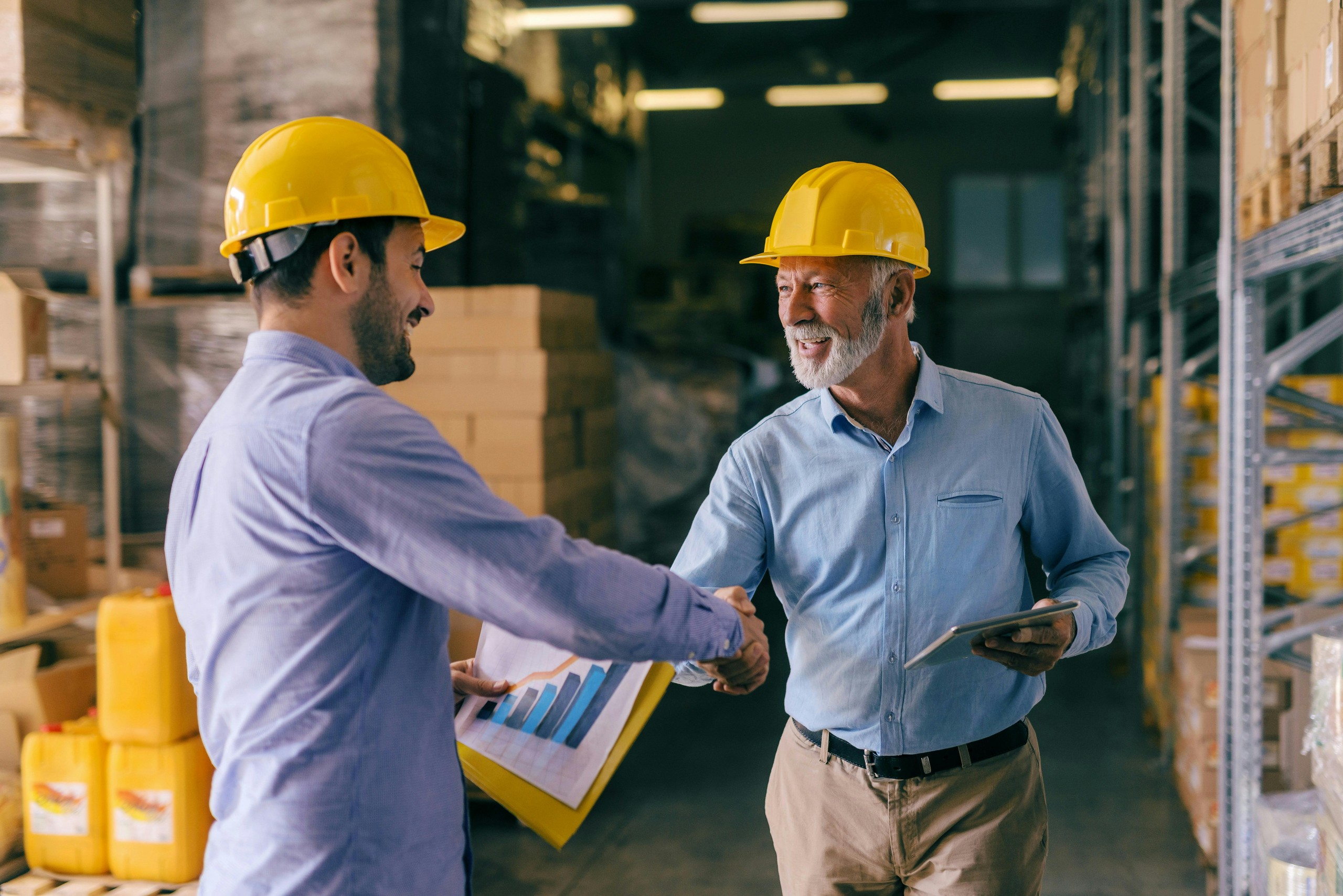 Two workers in hard hats shaking hands in a warehouse.