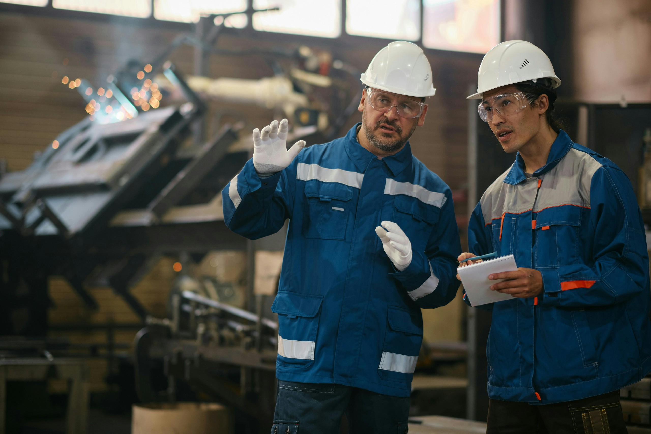 Senior worker instructing younger employee in factory