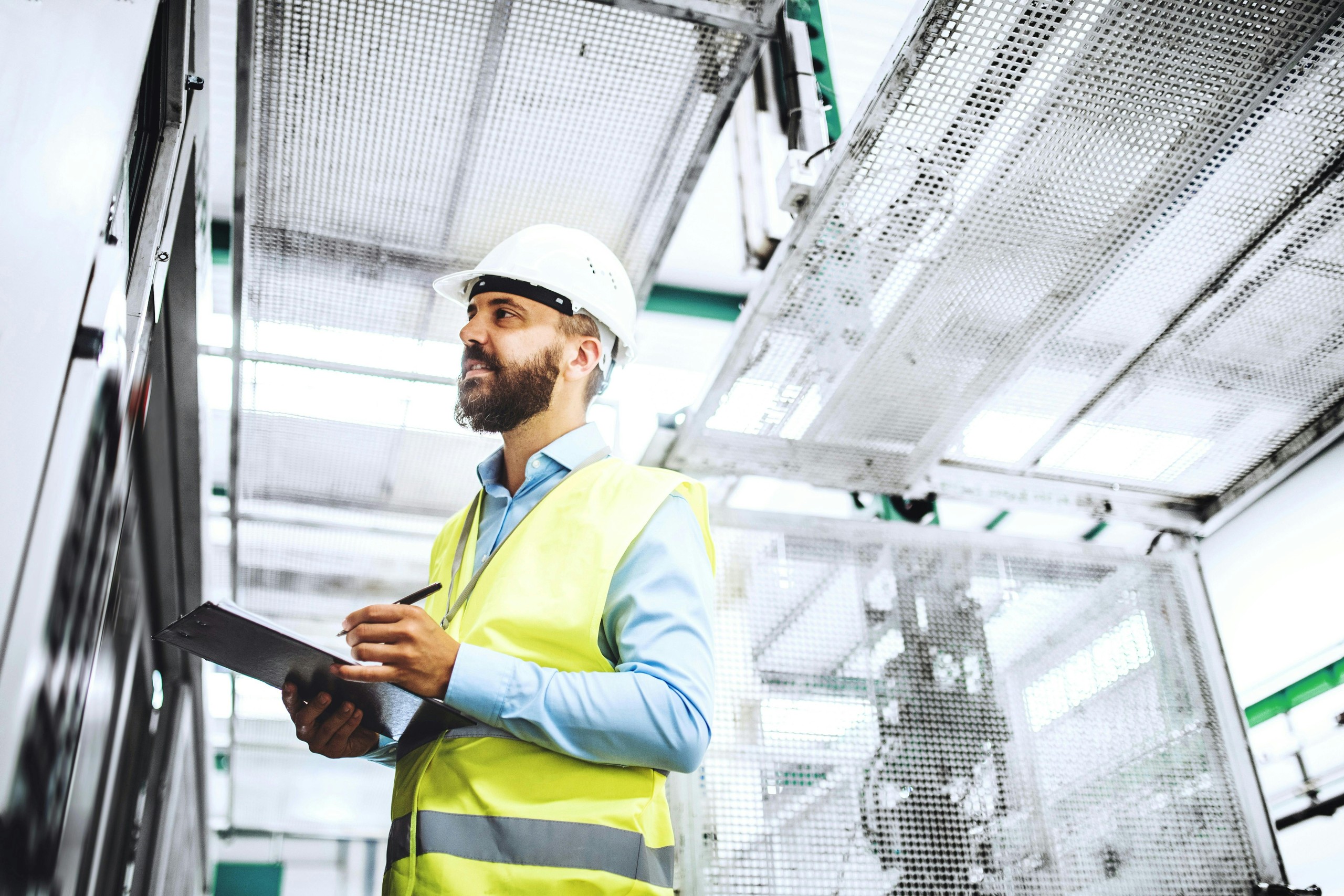 Worker in a hard hat writing on a clipboard in a factory