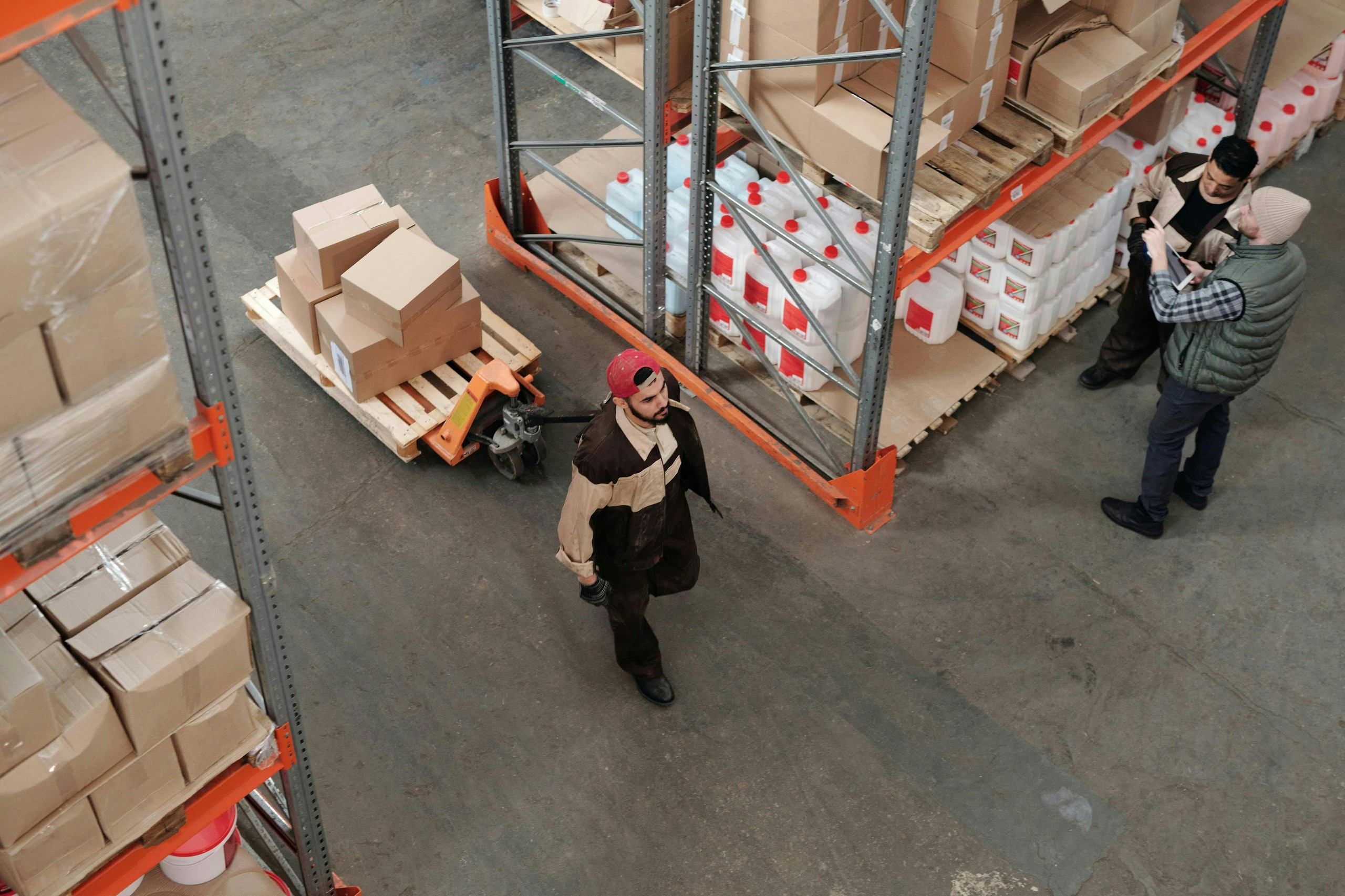 Three workers among stocked warehouse shelves.