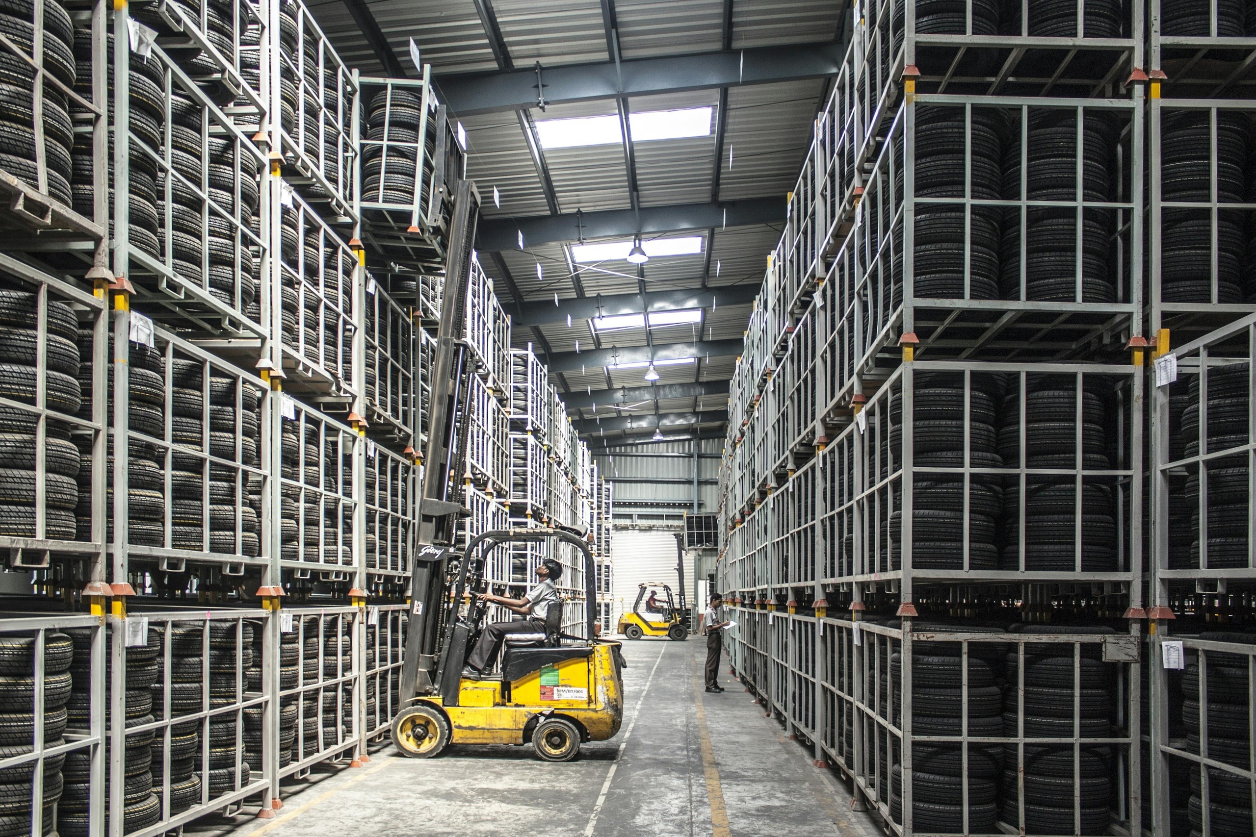 Forklift operator working between tall racks of tires in a warehouse.