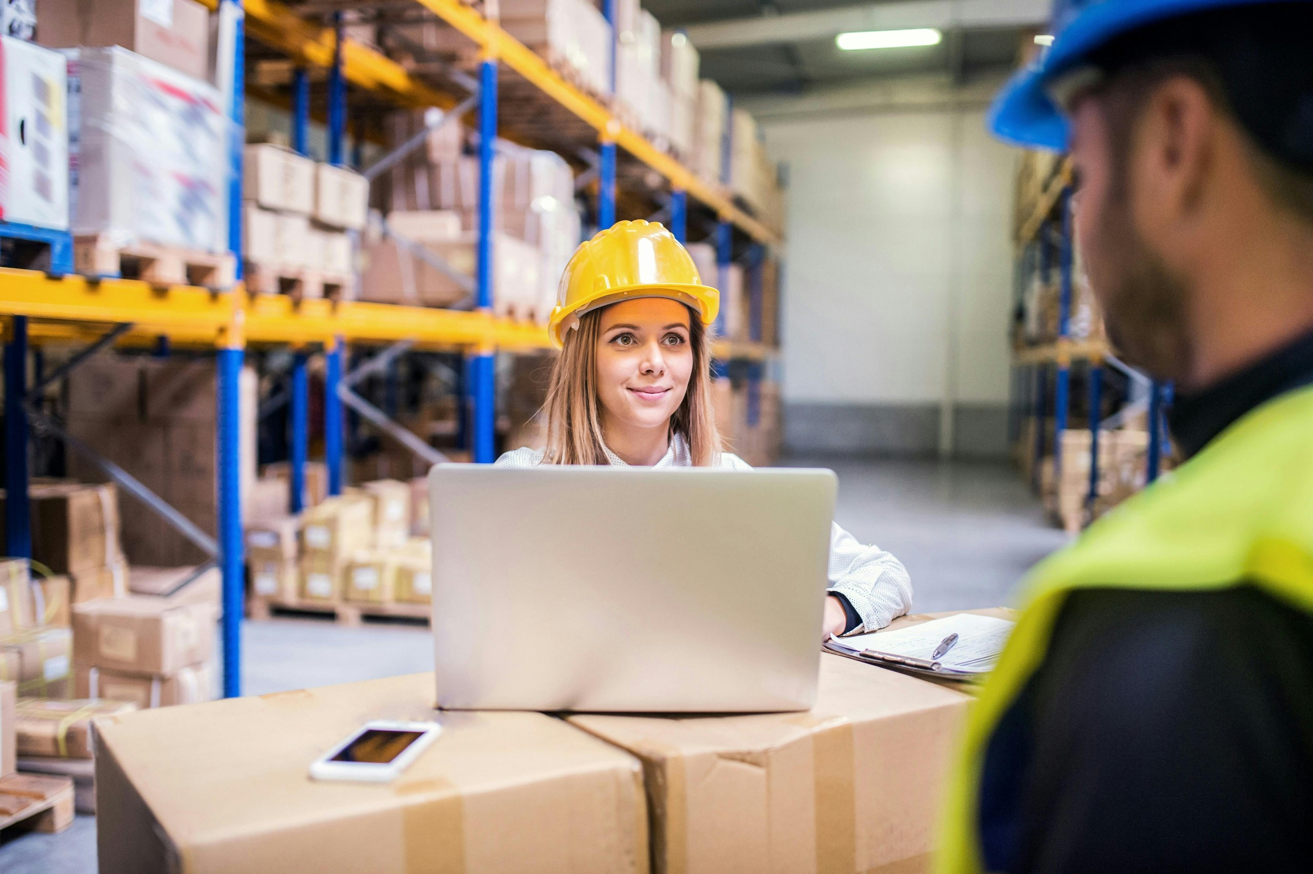 Warehouse manager and worker reviewing laptop in distribution center