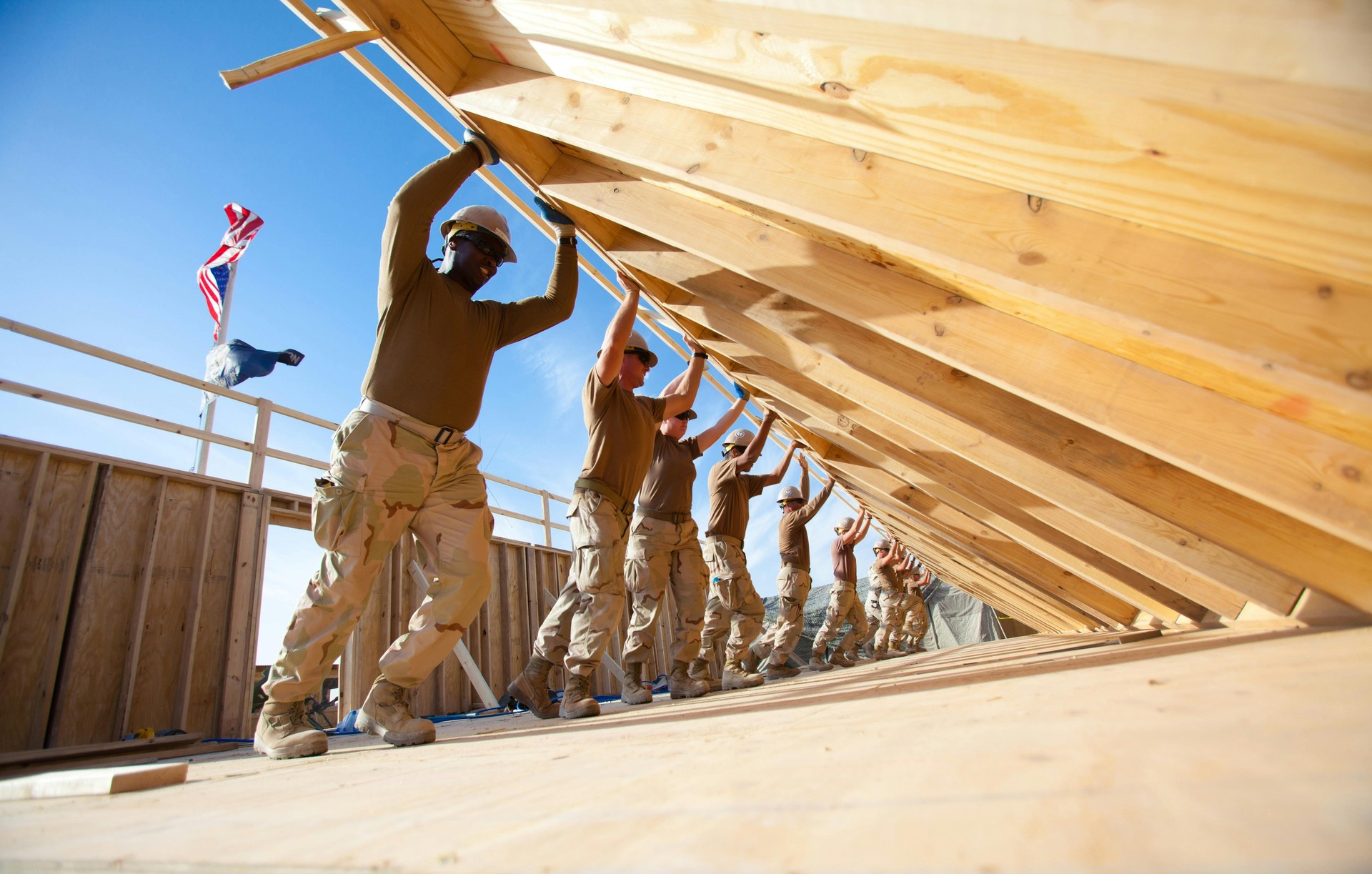 Construction crew in hard hats lifting a wooden wall frame together.