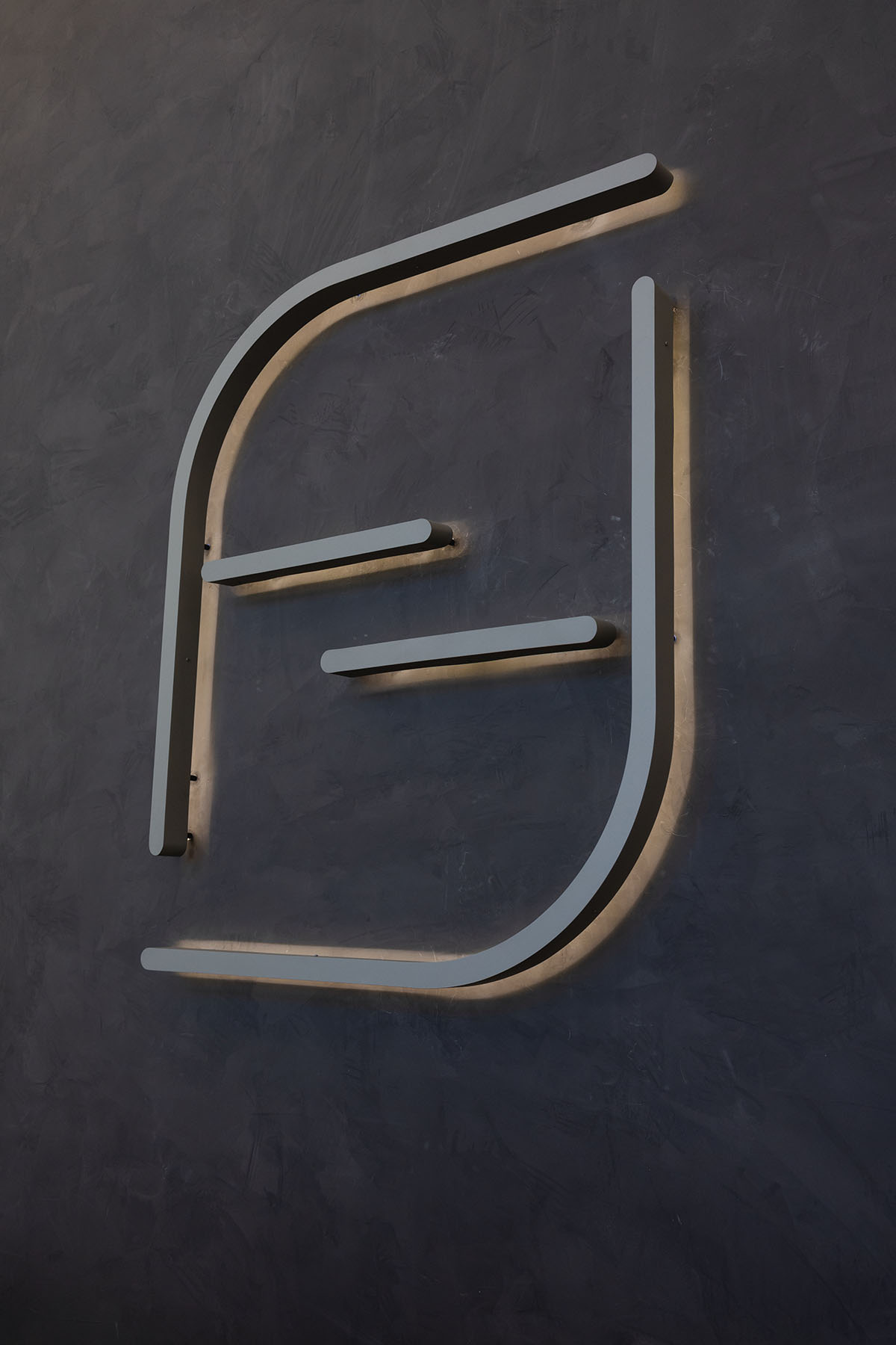 Modern abstract light fixture with curved gray bars mounted on a dark textured wall.