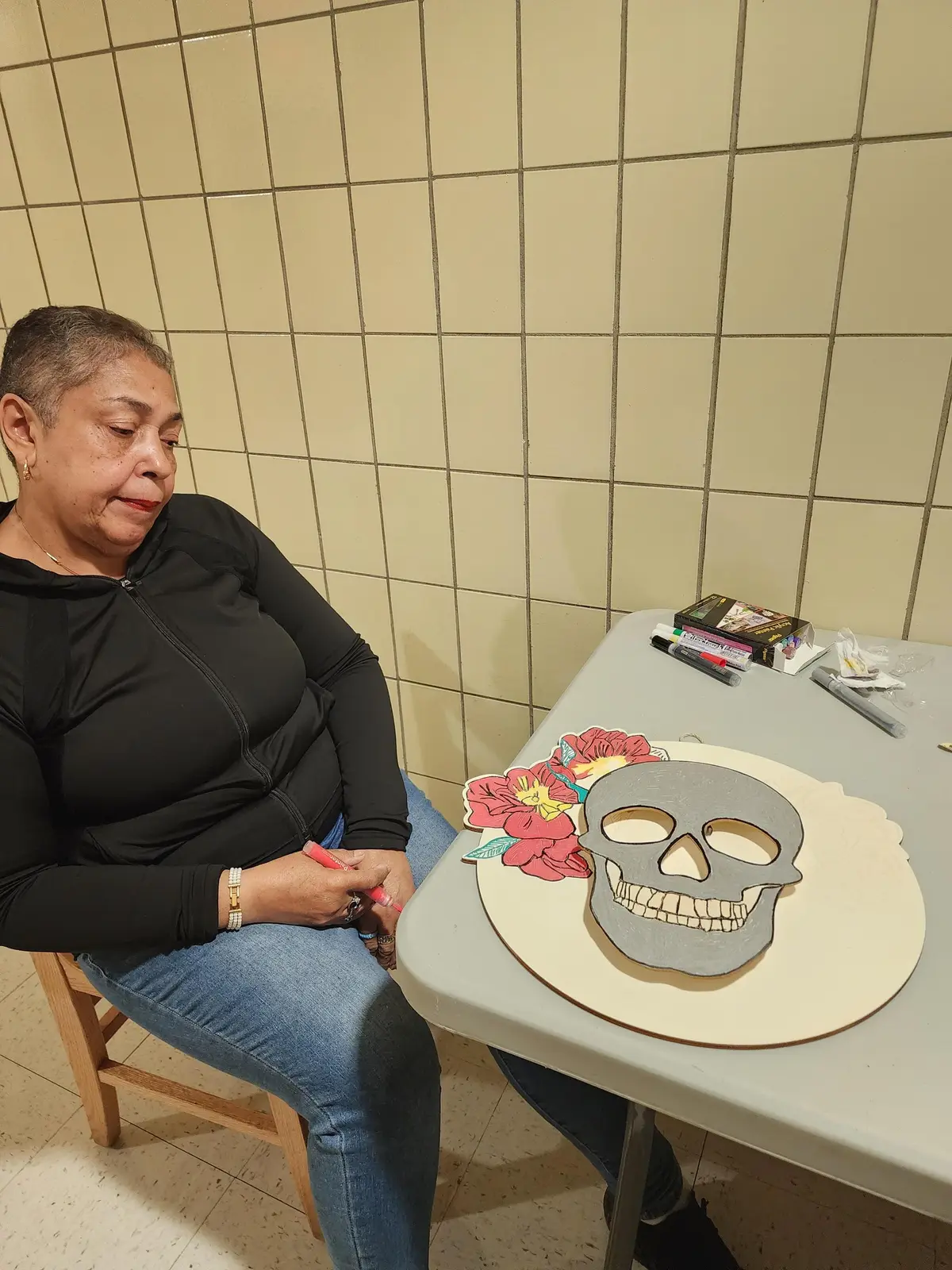 Adult decorating a wooden skull with flowers using markers