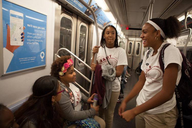 Students in school shirts talking and laughing on subway train
