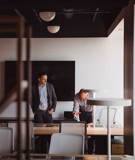 Two men in a modern office conference room reviewing documents on a long table.