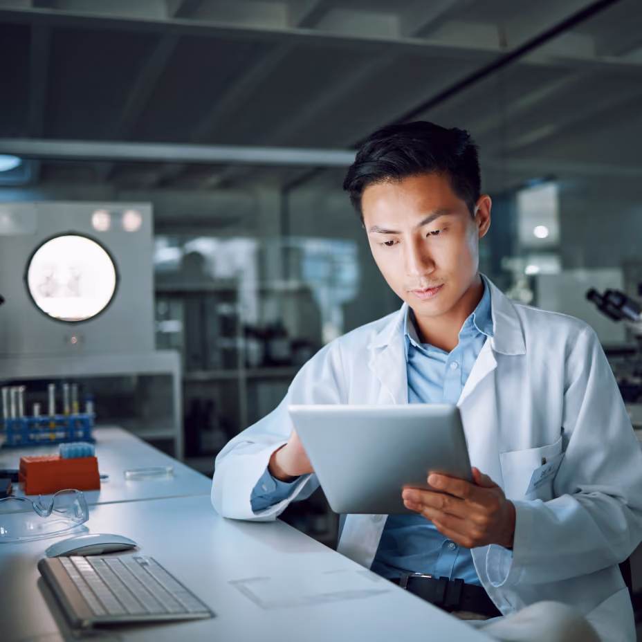 Scientist in a lab using a tablet, with lab equipment in the background.
