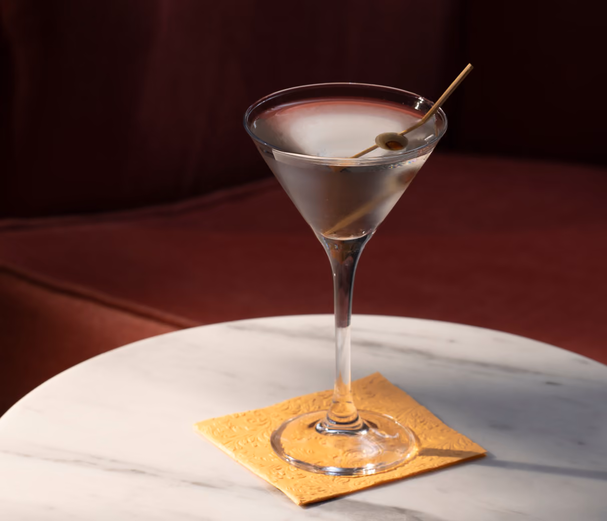 Martini cocktail on a marble table with red velvet seating.