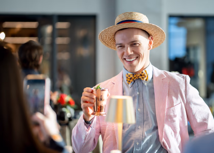 Smiling man in a pink suit and straw hat holding a drink.