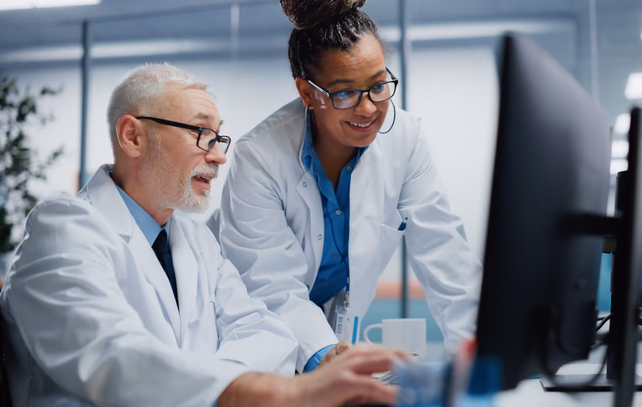 Two healthcare professionals collaborating at a computer in a modern medical office, reviewing patient information or clinical software together.