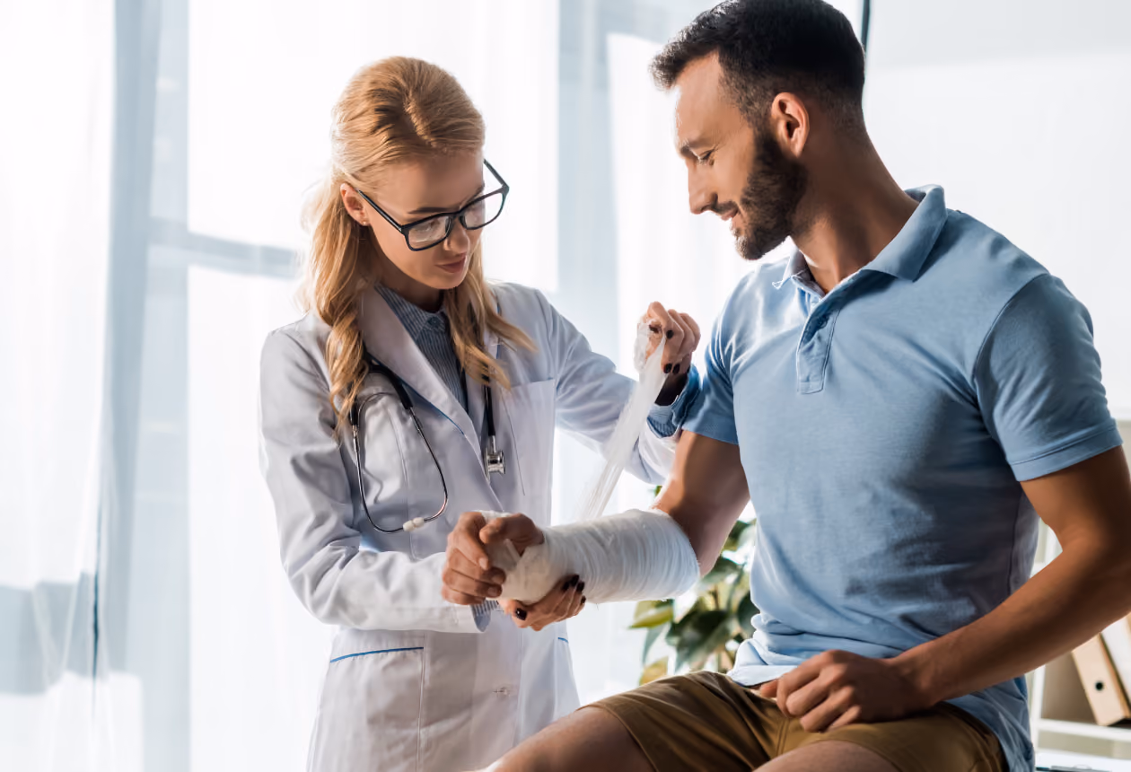 Healthcare professional applying a bandage to a male patient's injured forearm during a medical examination.