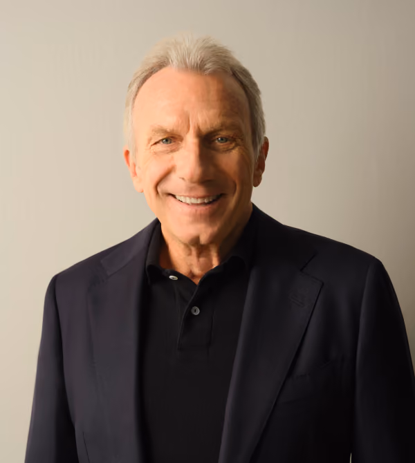 Portrait of legendary NFL quarterback Joe Montana smiling in a dark blazer and black shirt.