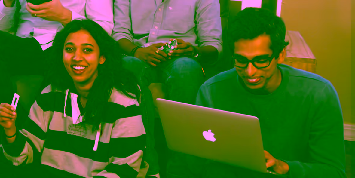 Two people sitting together, one holding a card and one using a laptop.