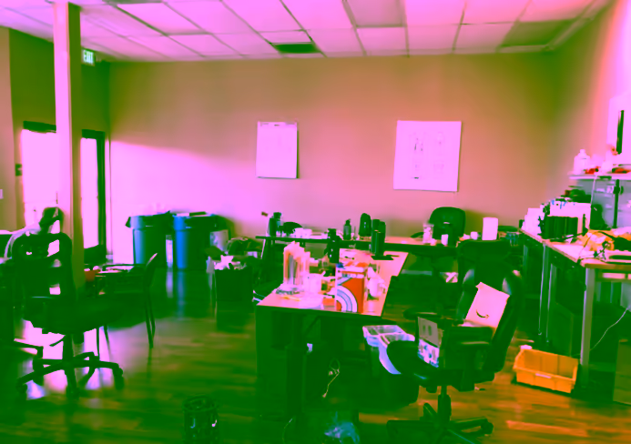 Cluttered office workspace with desks and chairs.