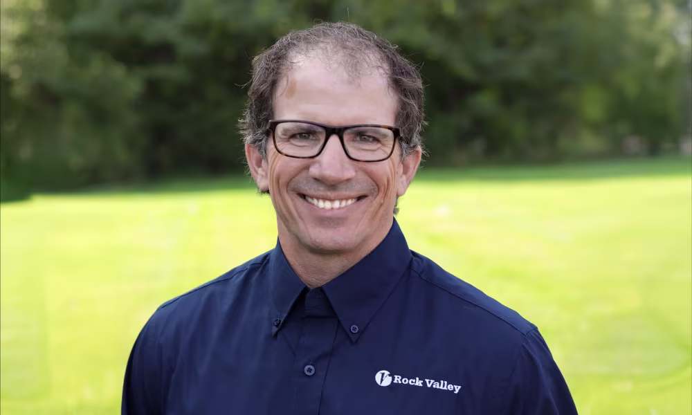 Smiling man wearing glasses and a blue polo shirt with Rock Valley logooutdoors.