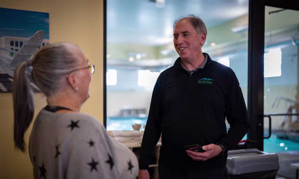 Two people smiling and talking inside a healthcare or therapy facility
