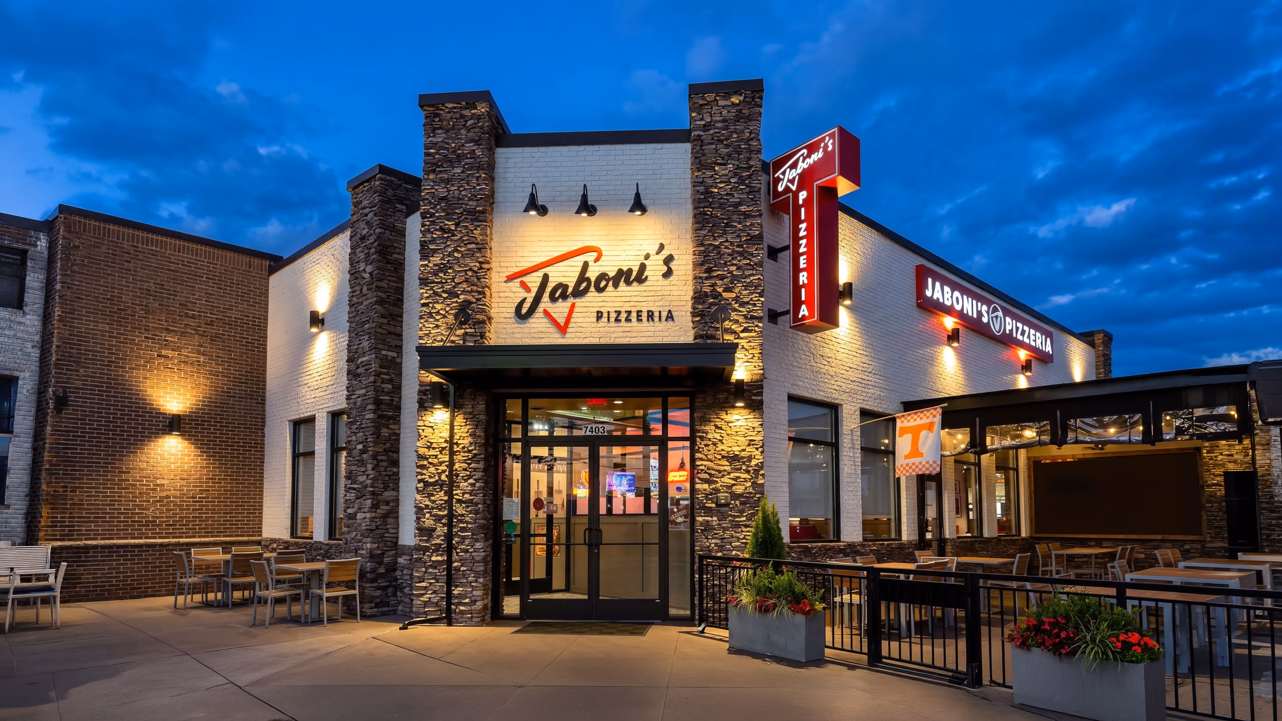 Exterior of Jaboni's Pizzeria at dusk with outdoor seating and illuminated signs.