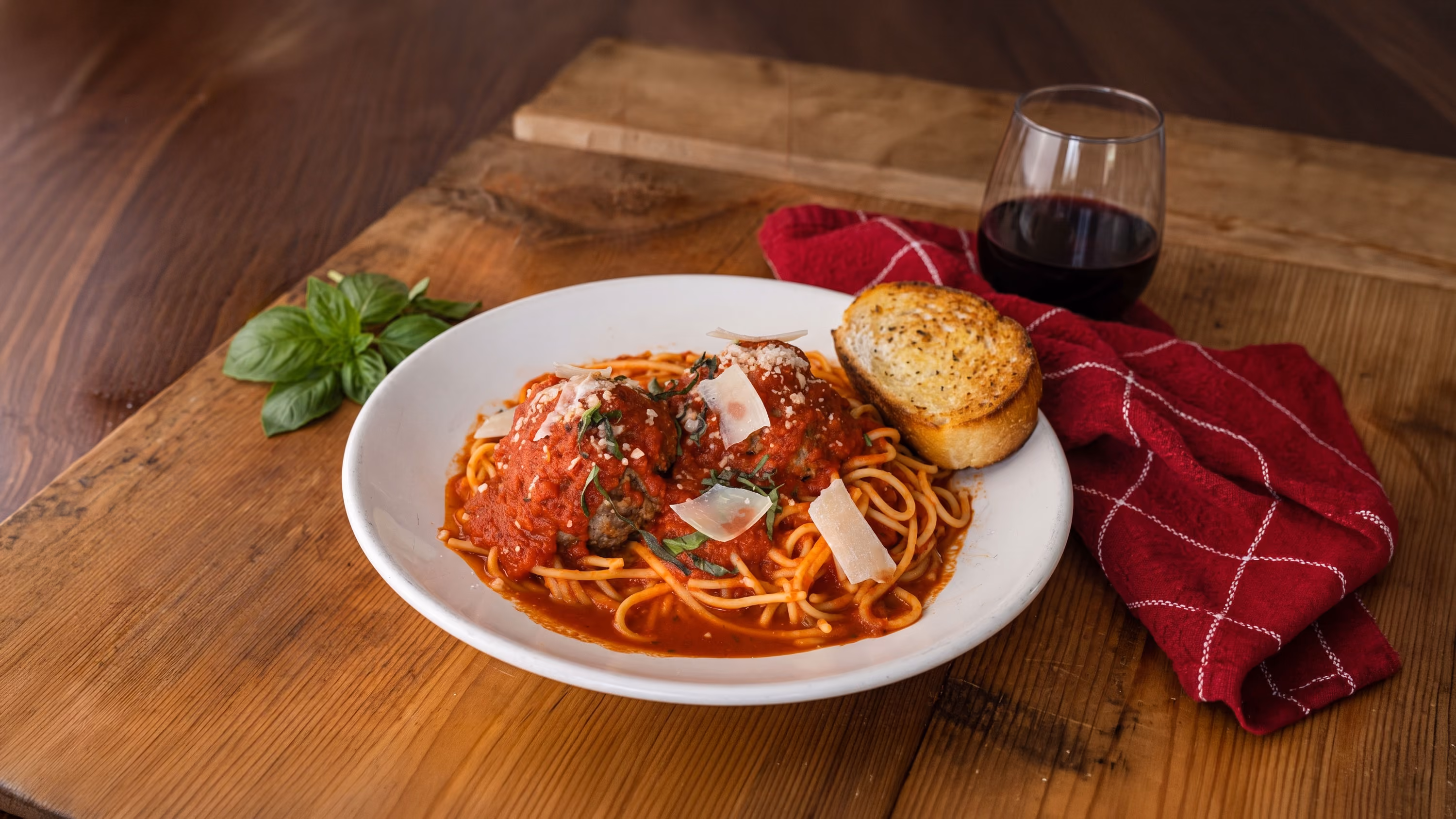 Plate of spaghetti with tomato sauce, meatballs, Parmesan, basil, garlic bread, and a glass of red wine.