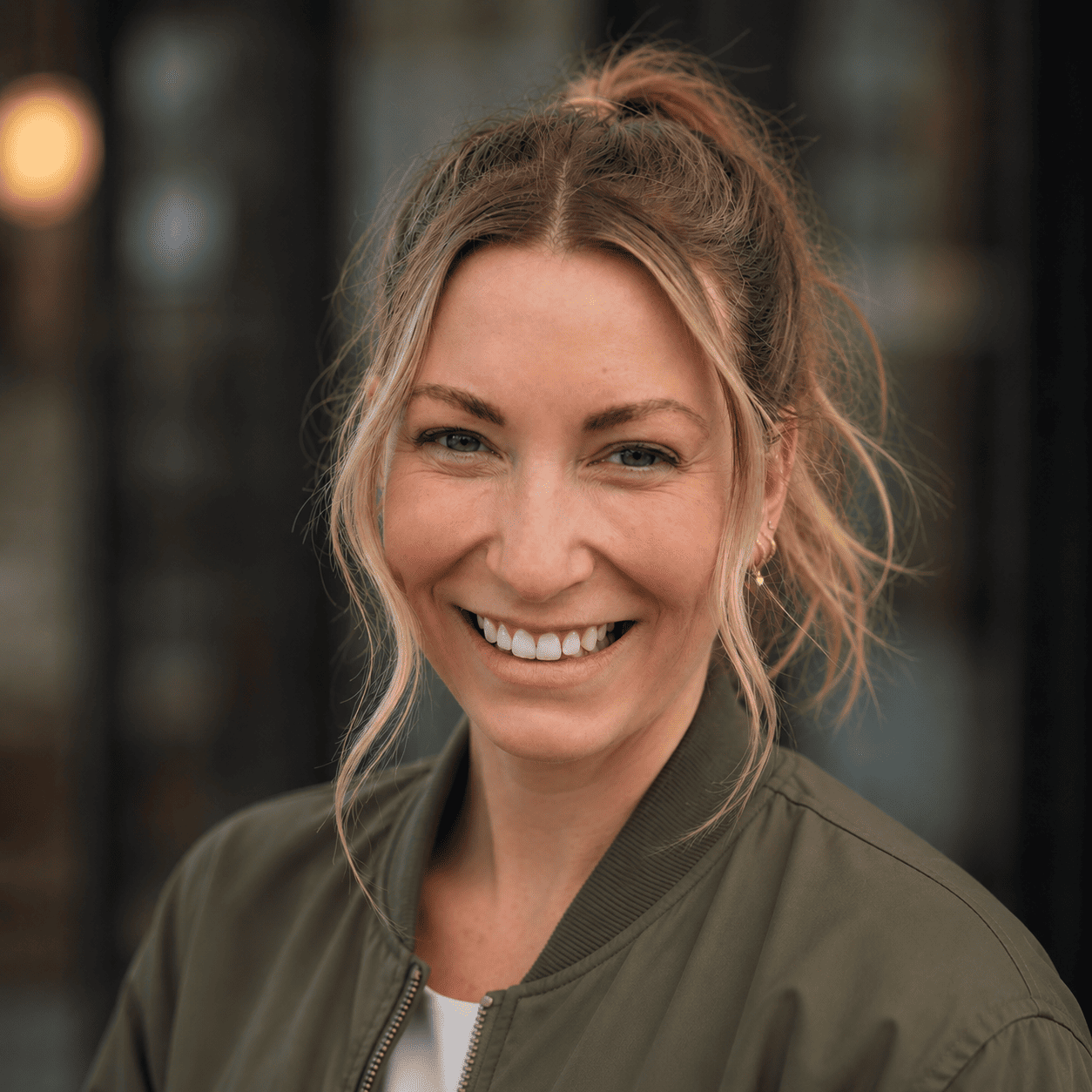 Bre Wihongi smiling, wearing an olive bomber jacket, with her hair pulled up