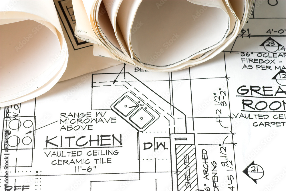 Close-up of architectural blueprint showing kitchen layout with sink, stove, and rolled-up plans.