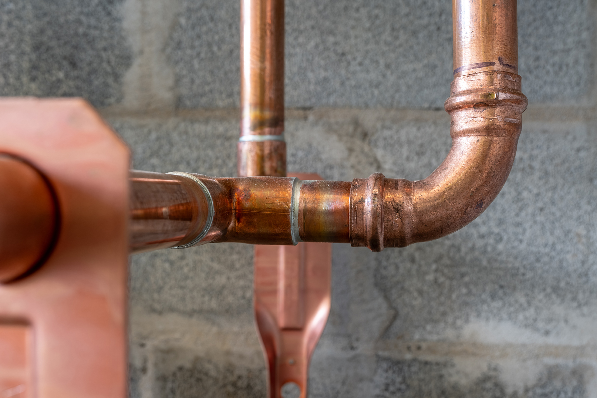Close-up of copper pipe fittings connected with joints against a gray cinder block wall.