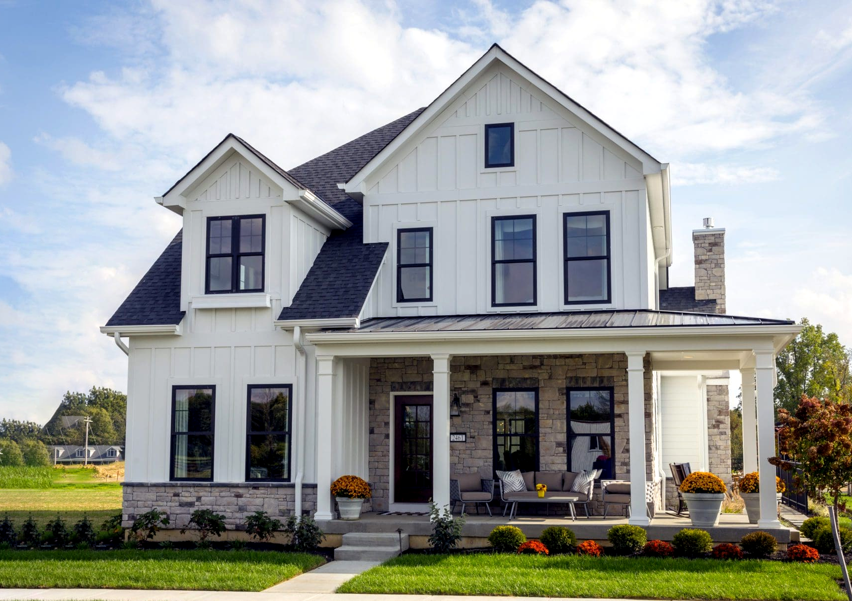 Two-story white house with black windows, stone accents, front porch with seating, and landscaped lawn.