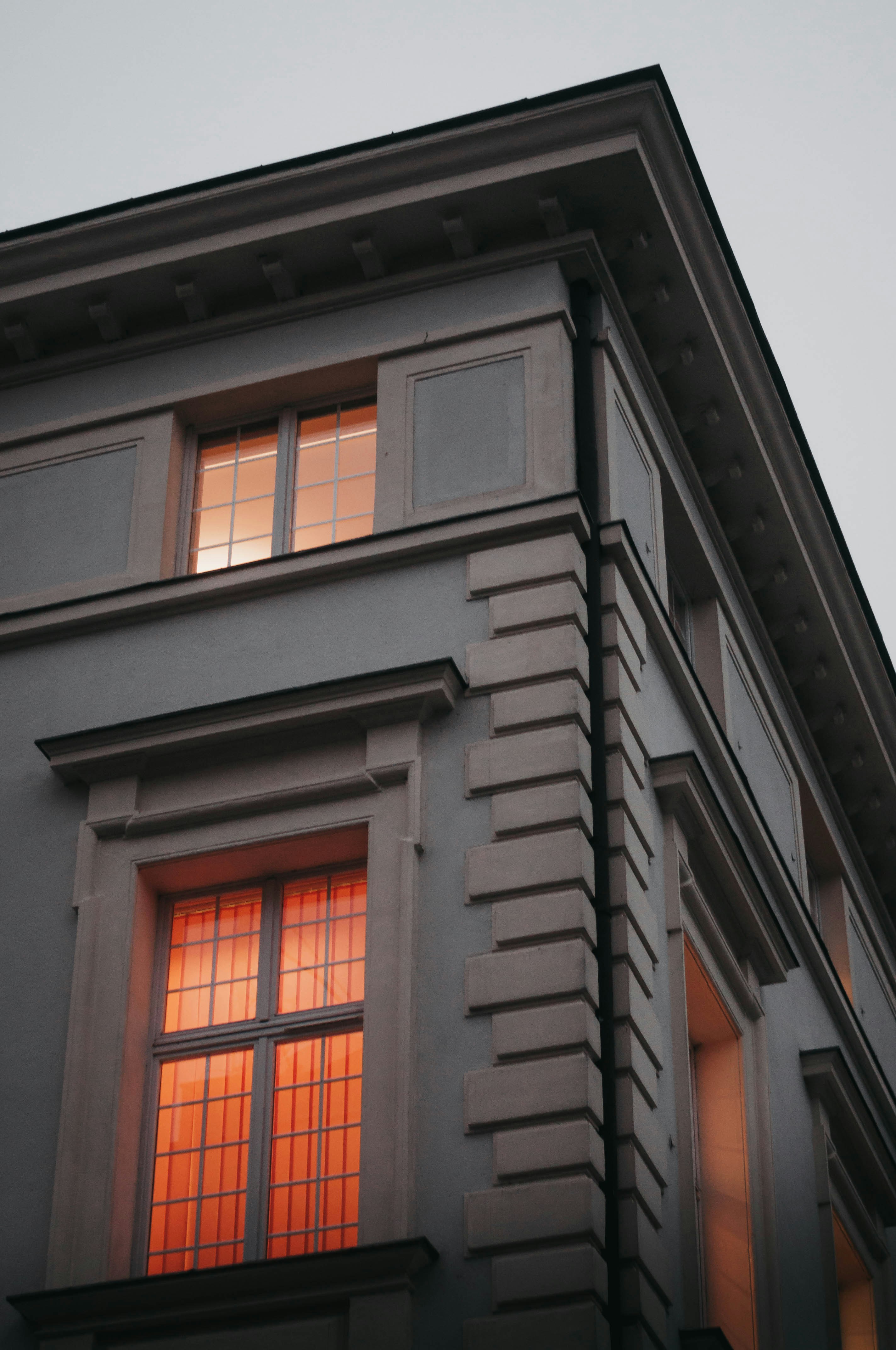 Corner of a gray building with illuminated windows glowing warm orange at dusk.