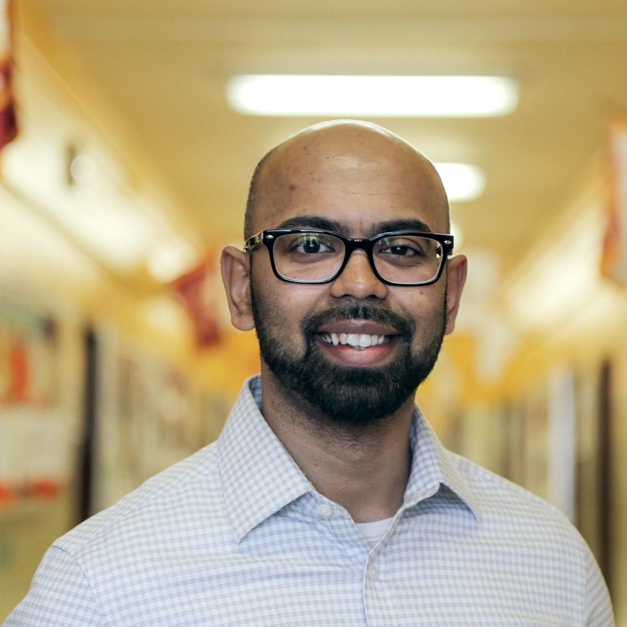 Mr. Roy smiling in a school hallway