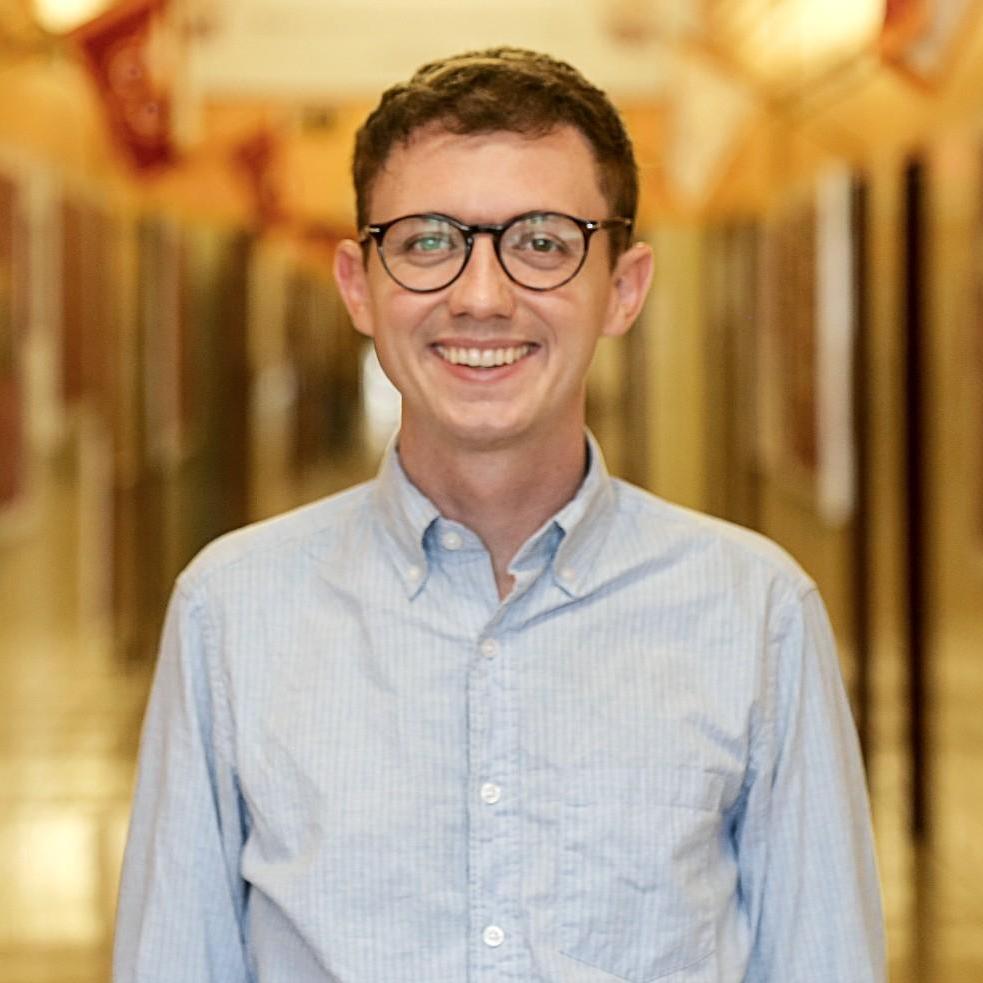 Mr. Burrell smiling in a school hallway wearing glasses