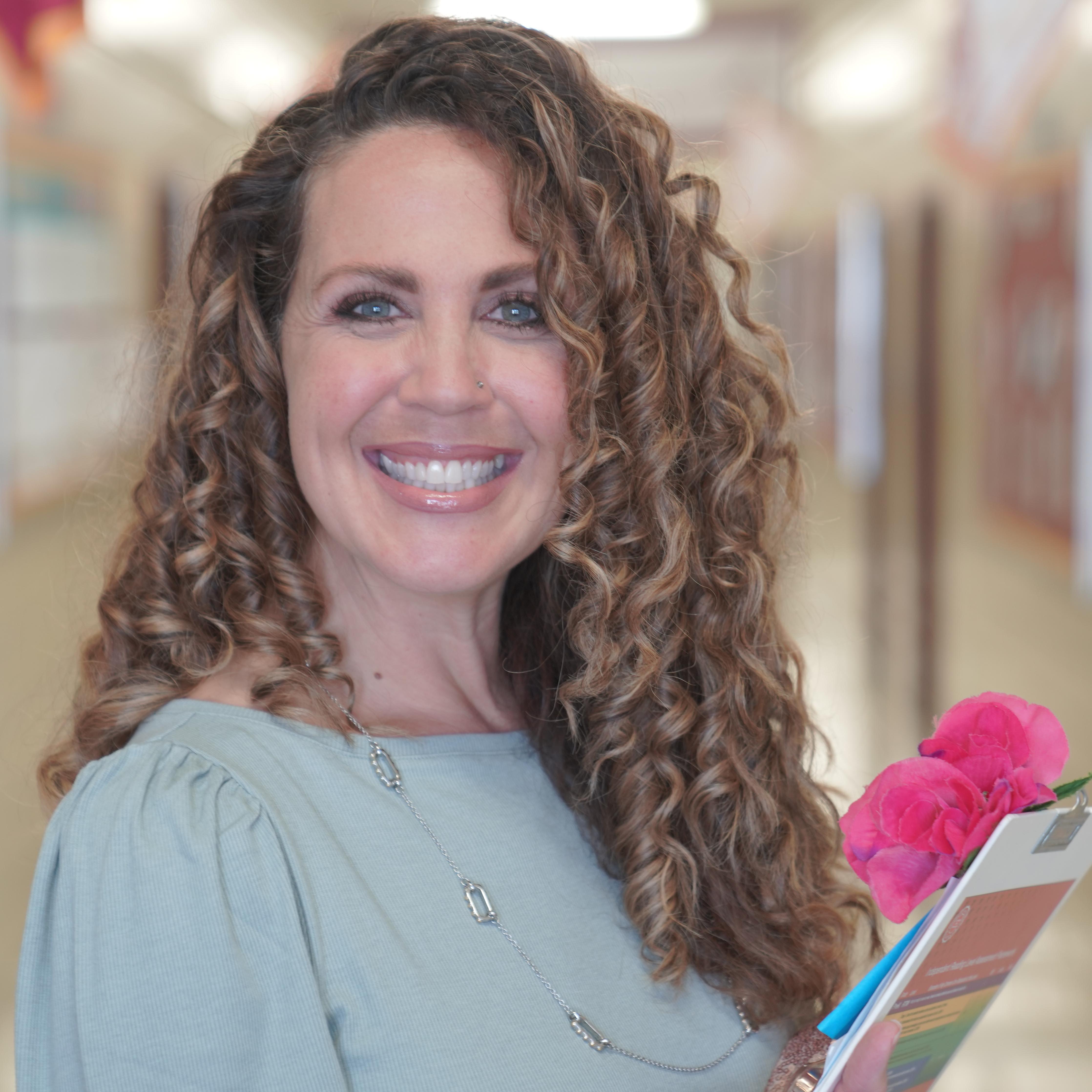 Dr. Callahan smiling in school hallway holding clipboard and flowers