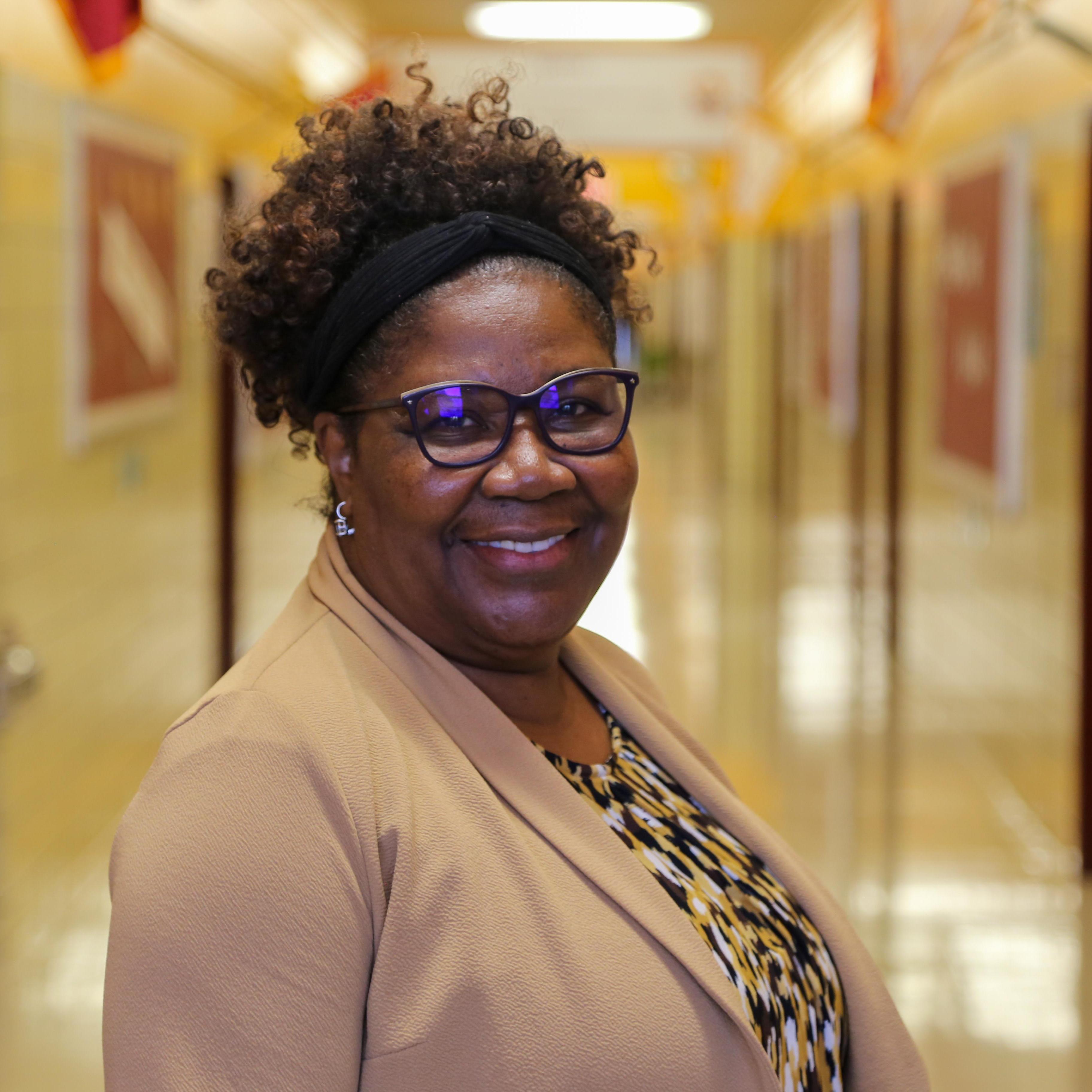 Ms. Fuller smiling in a school hallway wearing glasses