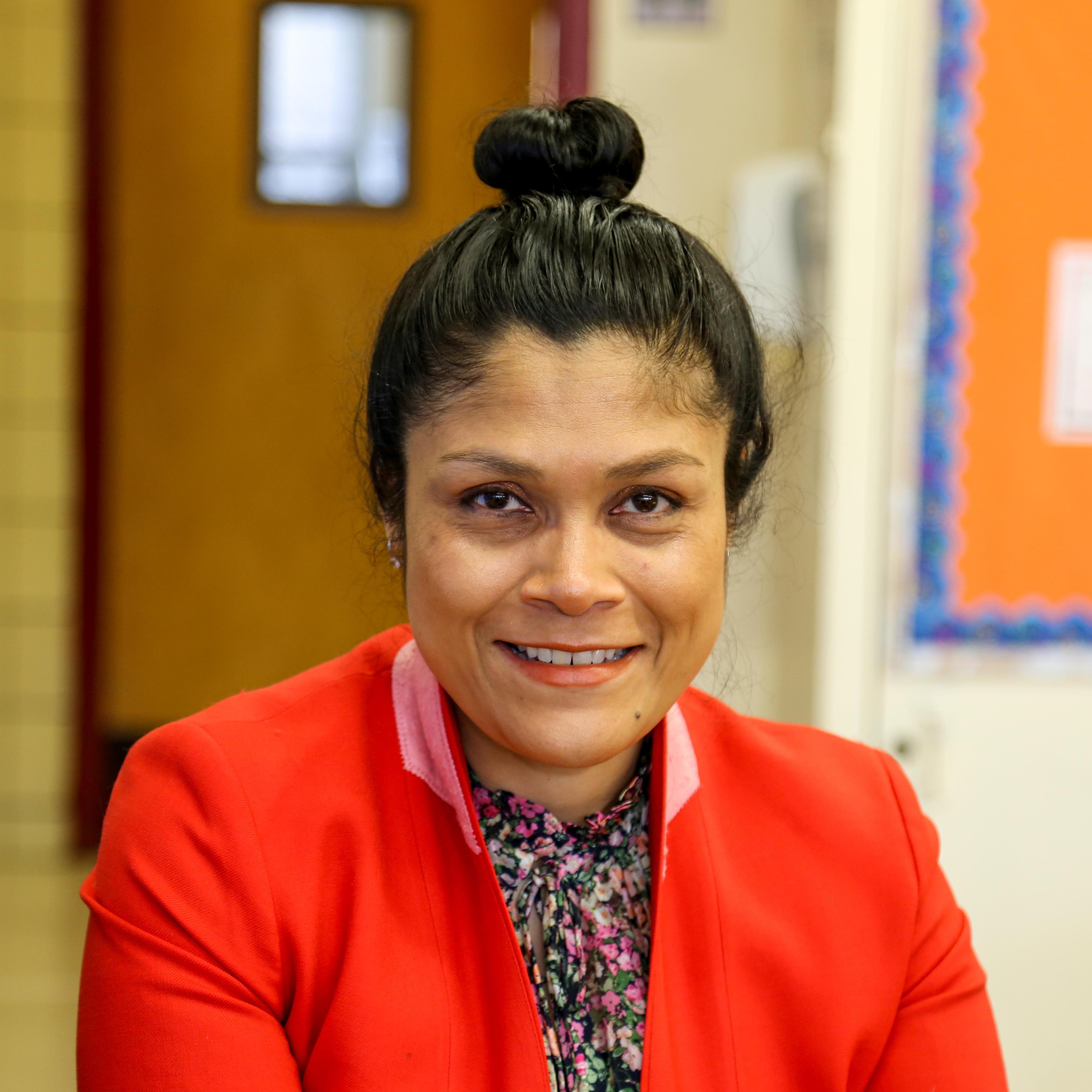 Ms. Hidalgo smiling in a school hallway wearing a red blazer
