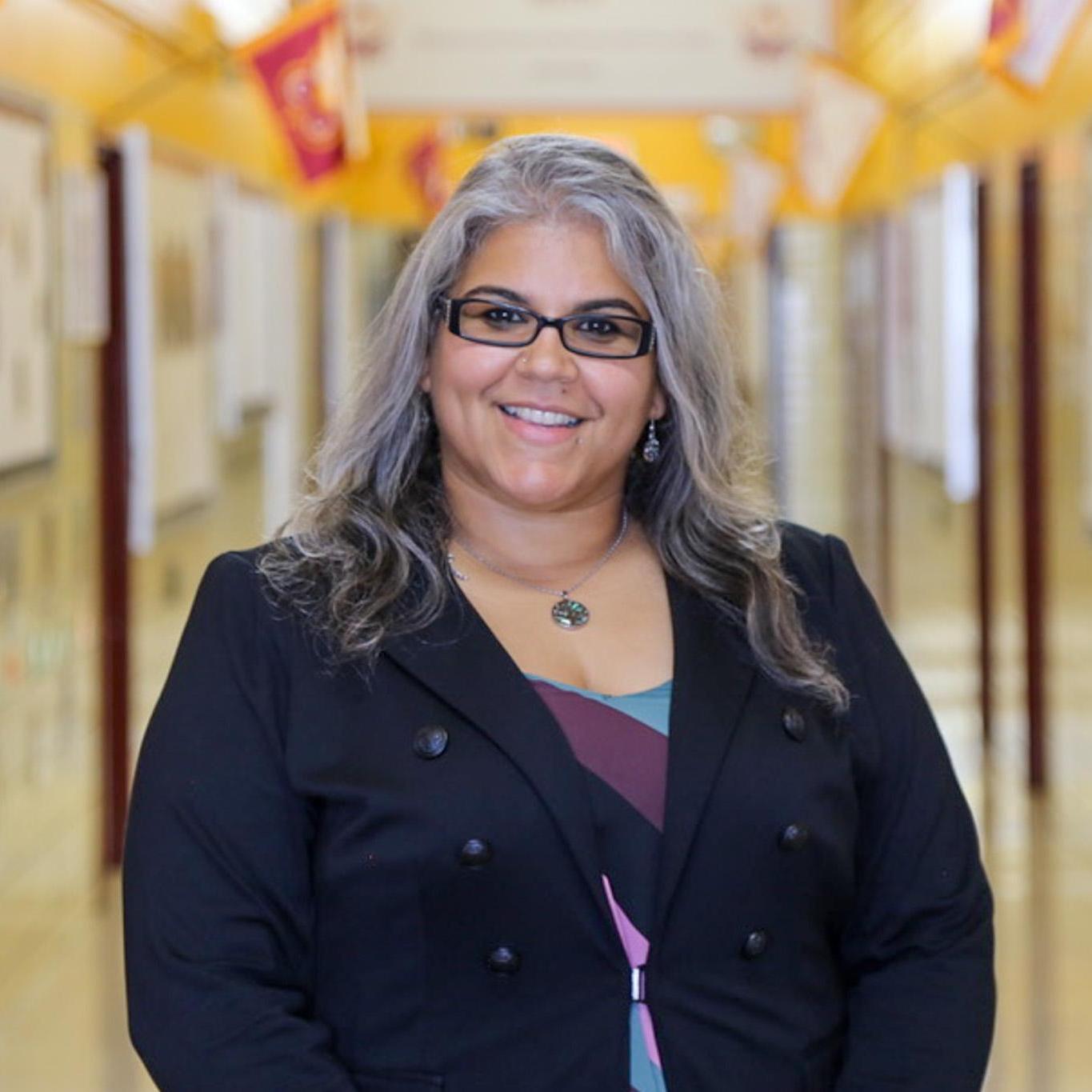 Ms. Palau smiling in a school hallway wearing a black blazer
