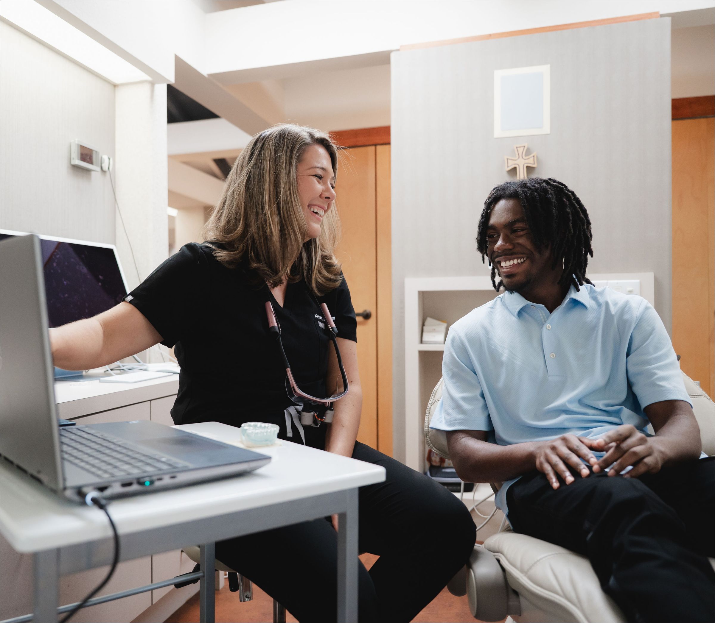 Team member showing a laptop screen to a smiling patient in the exam room.