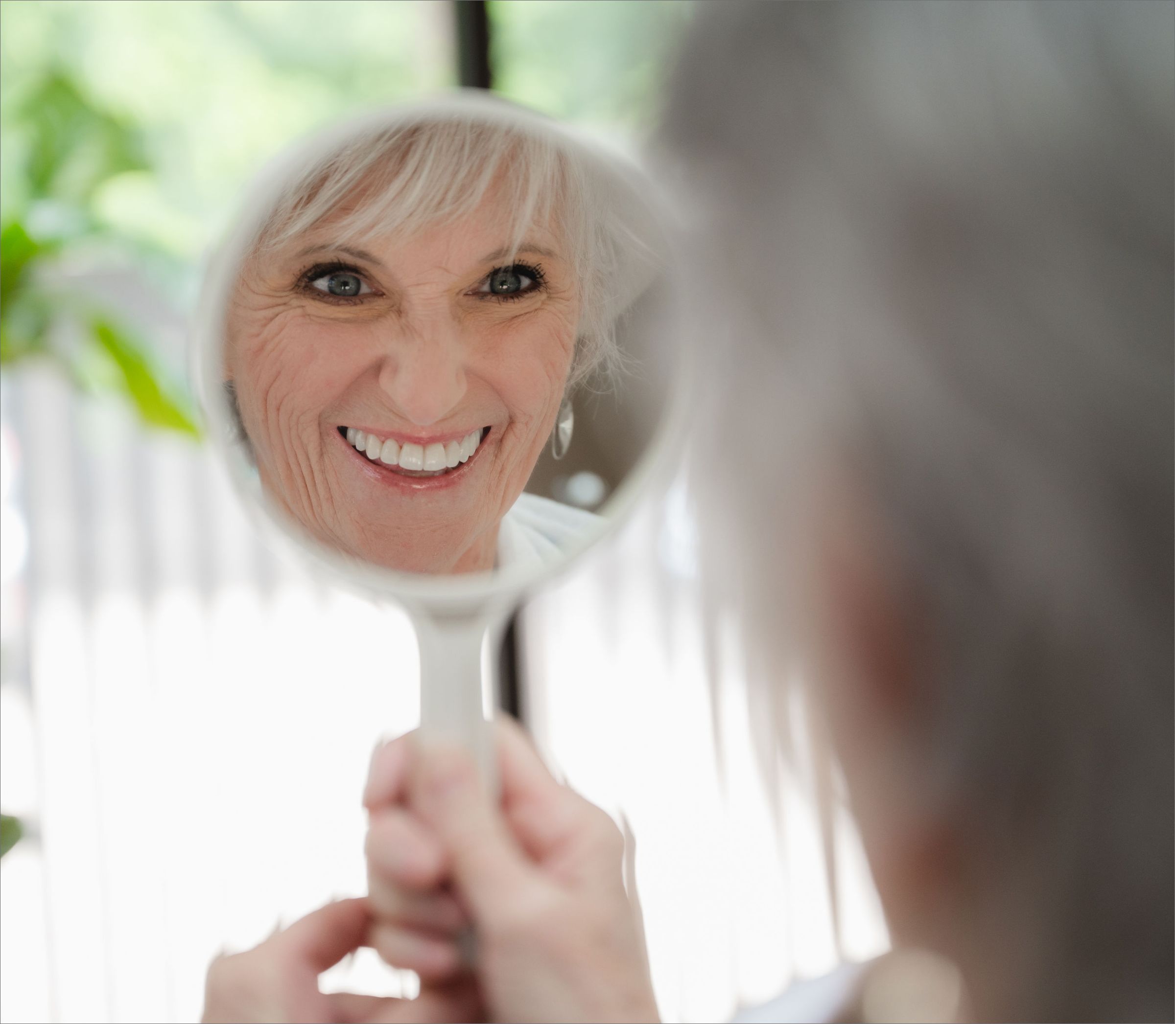 Smiling senior patient looking at her reflection in a hand mirror.