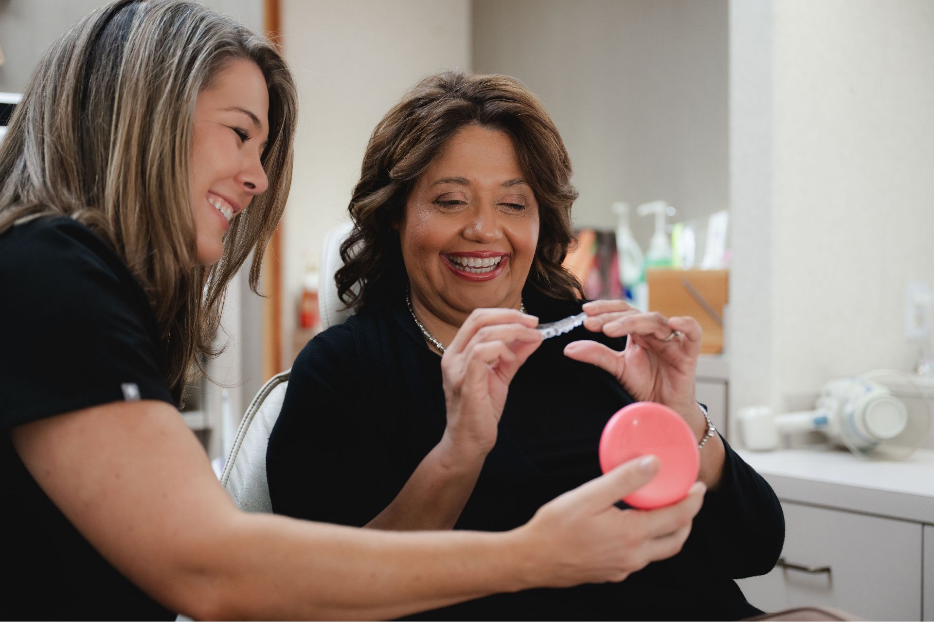 Two smiling team members looking at a clear dental aligner.