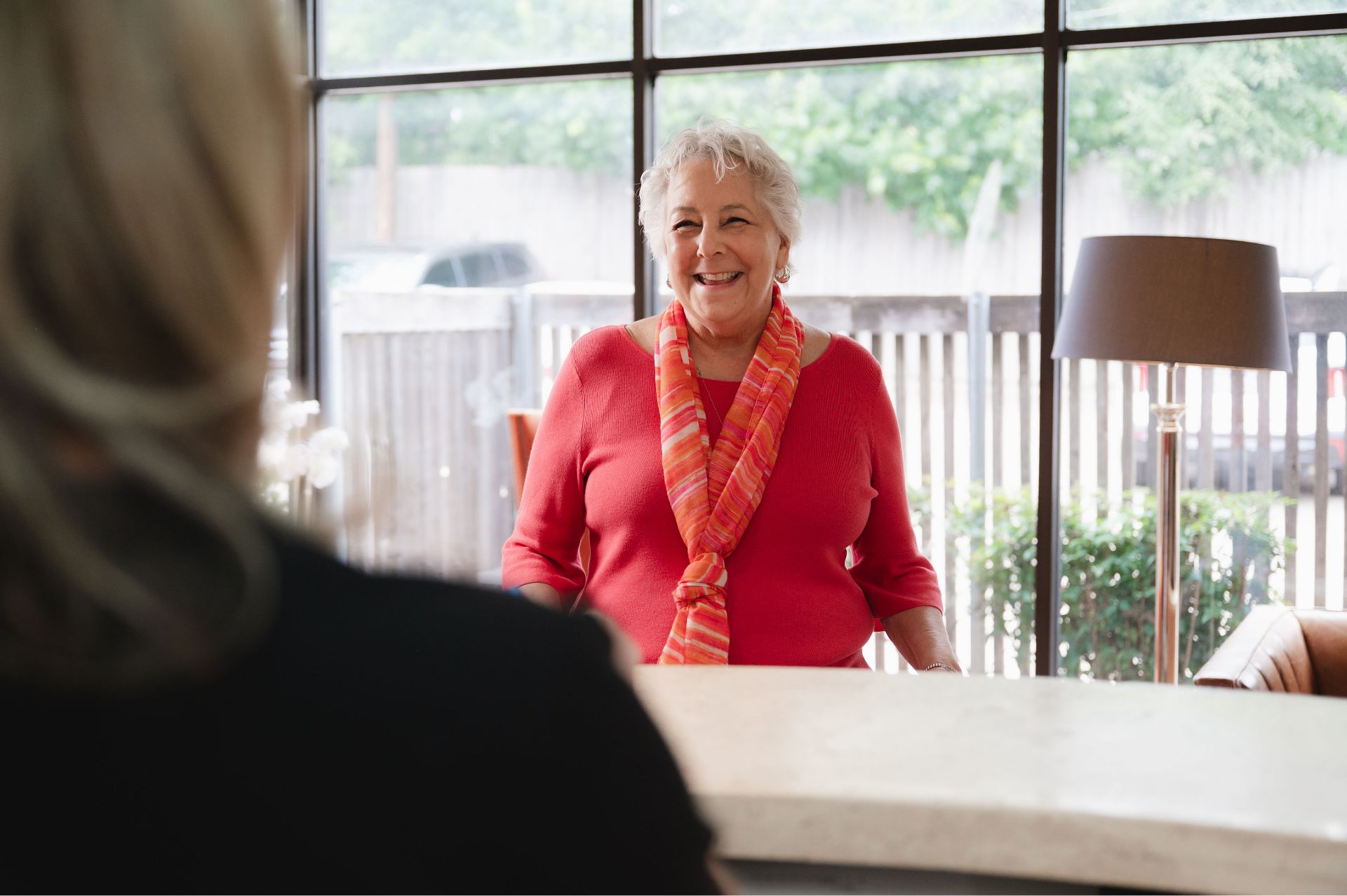 Smiling patient in a red top greeting a team member at the front desk.