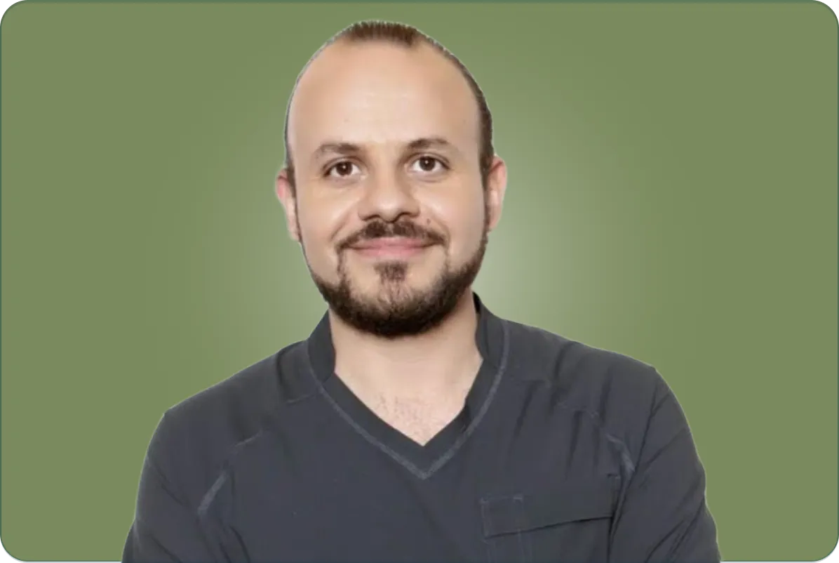 Smiling man with a beard and pulled-back hair wearing a dark shirt against a green background.