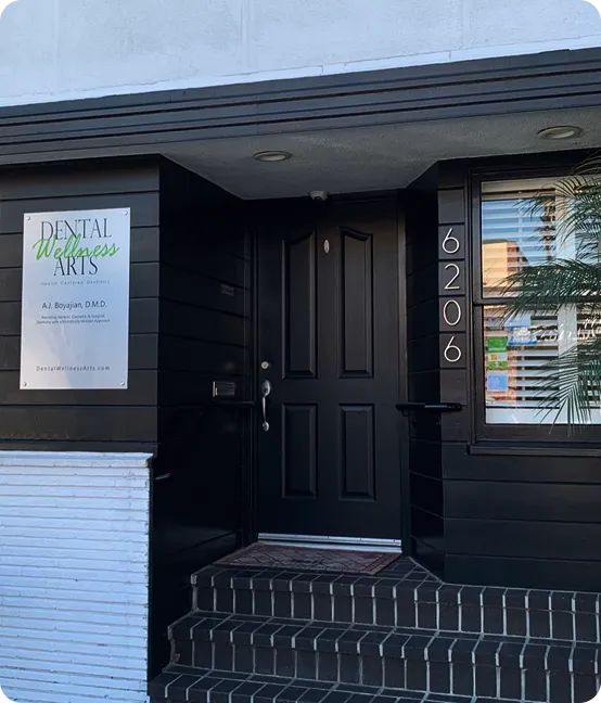 Entrance to Dental Wellness Arts office with black door, steps, and address number 6206 on wall.