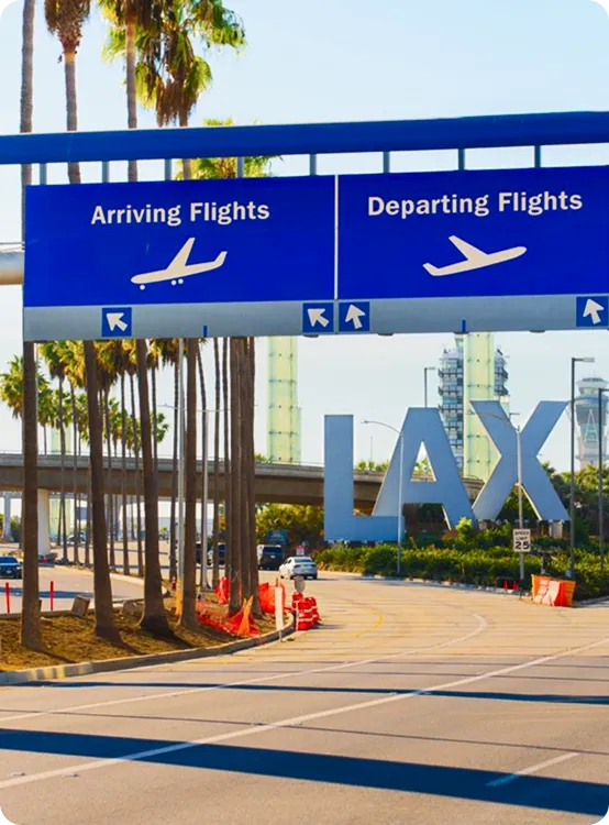 Road signs directing to arriving and departing flights near large LAX airport letters and palm trees.