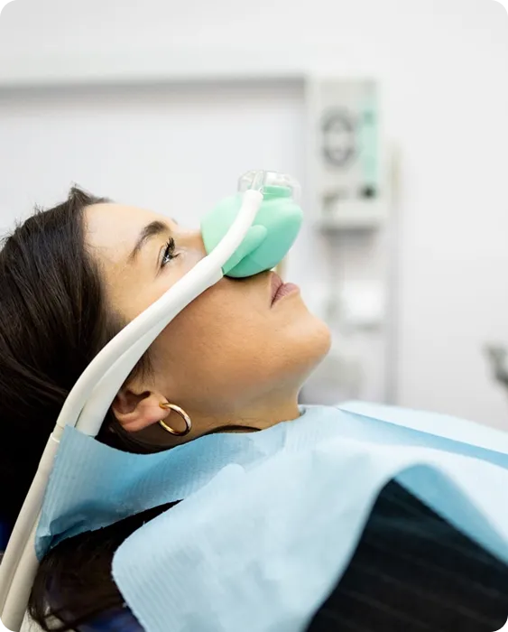 Woman receiving dental sedation with a green nose mask while lying back in a dental chair.