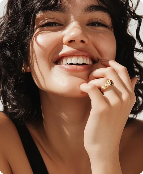 Close-up of a smiling woman with curly hair resting her chin on her hand showing a gold ring.