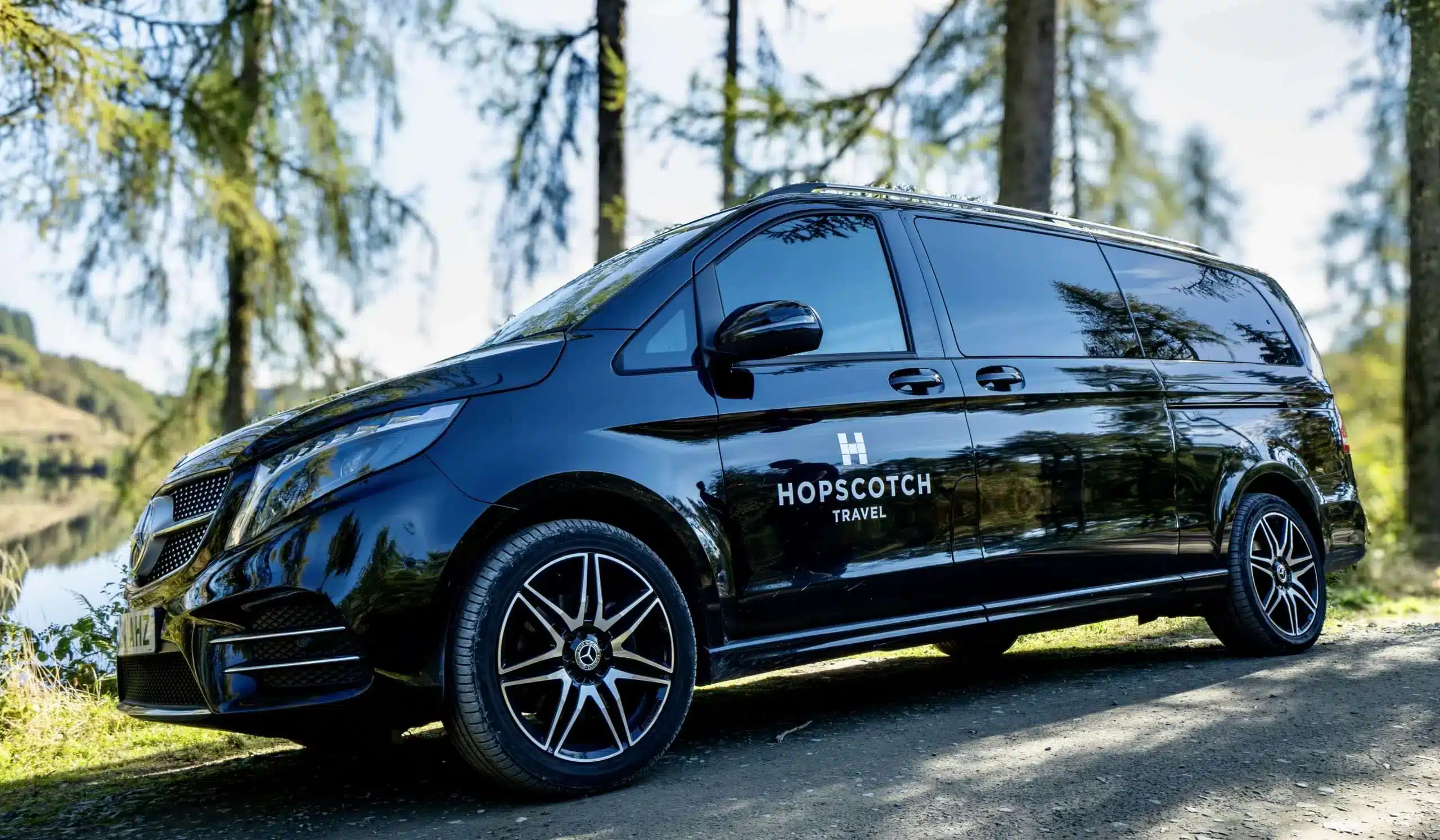 Hopscotch Travel luxury Mercedes tour van parked in a forest beside a loch