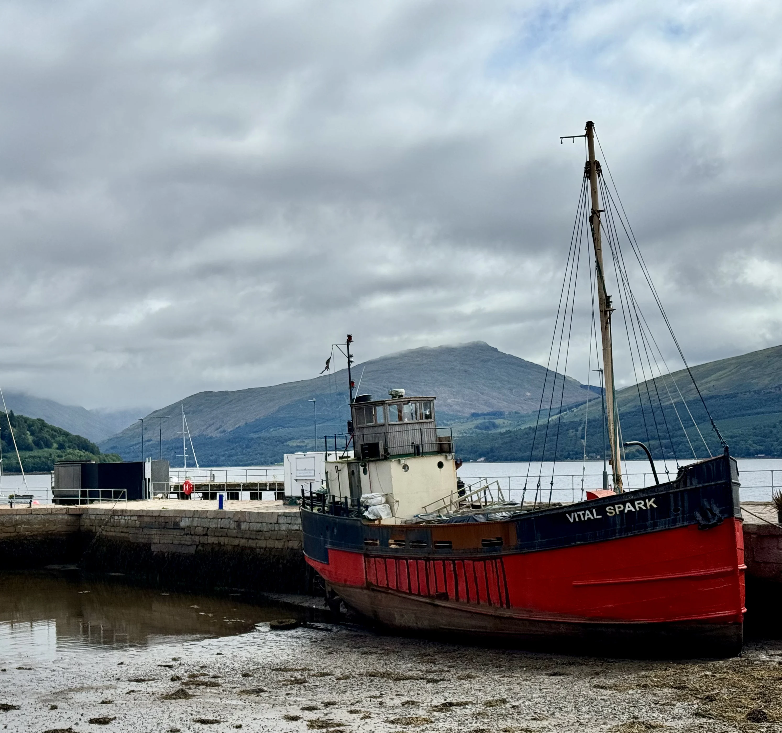 Red and black fishing boat moored in Scottish highland loch with mountains behind